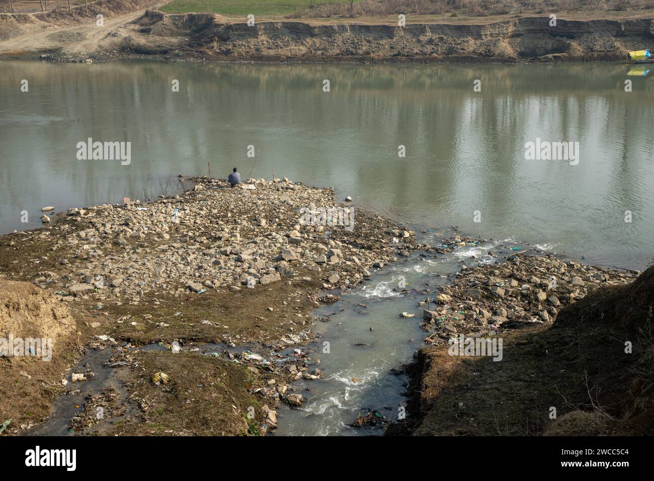 Ein Mann aus Kaschmir sah an einem kalten Wintertag in Srinagar auf dem teilweise getrockneten Teil des Flusses Jhelum fischen. Eine beispiellose Trockenheit inmitten der intensiven Kälte hat dazu geführt, dass viele Gewässer in Kaschmir auf den Grund treffen, da das Wetterbüro bis zum 25. Januar im Allgemeinen trockenes Wetter vorhersagt. Wetterbeamte gaben an, dass die Region derzeit von einer außergewöhnlichen Dürre heimgesucht wird, mit einem Niederschlagsdefizit von 80 % ab Dezember 2023. Das anhaltende trockene Wetter hat jedoch bei den Menschen, die mit Landwirtschaft und Gartenbau in Verbindung stehen, ernste Besorgnis erregt, da Experten diese Wetterschiefe miteinander verbinden Stockfoto