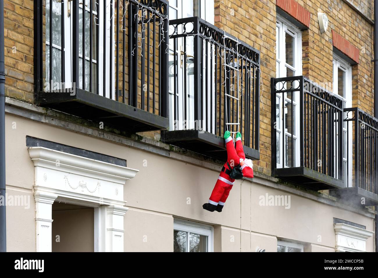 Ein hochgejagter Weihnachtsmann hängt von einem Balkon der Wohnung, als würde er versuchen, eine Leiter hinaufzuklettern, um Zugang zu den Räumlichkeiten zu erhalten, Surrey England UK Stockfoto