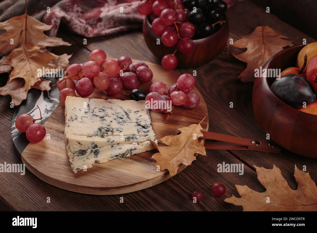 Käseplatte mit Herbstfrüchten und trockenen Blättern Stockfoto