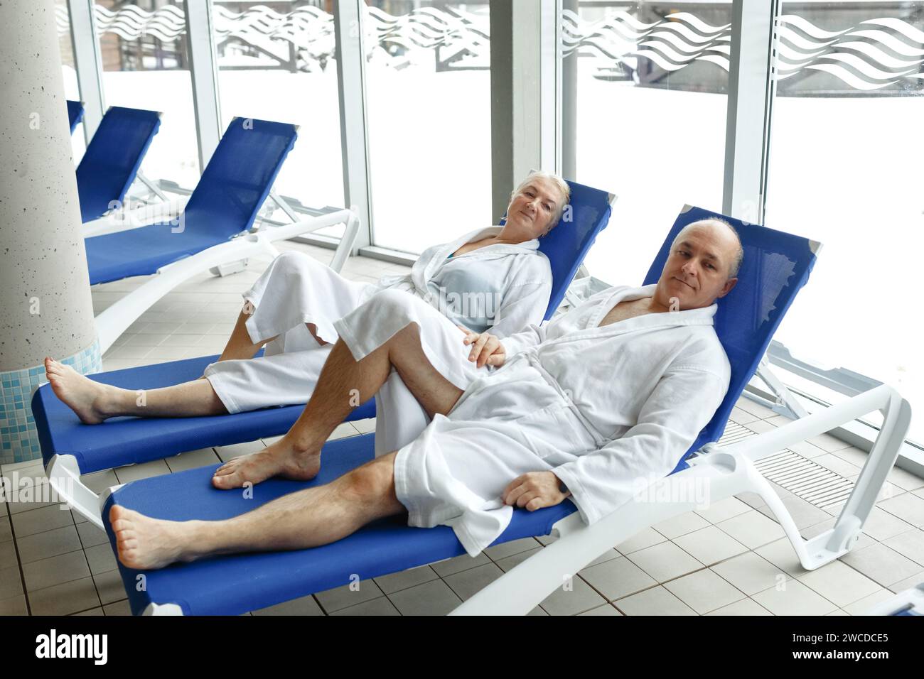 Eine ältere Frau mit einem Mann in Bademänteln auf einer Liege am Pool. Entspannen Sie sich im Spa-Center. Stockfoto