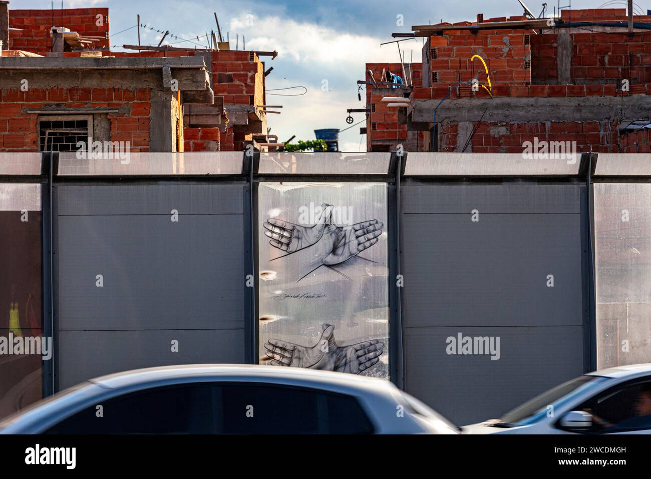 Complexo da Mare, ein riesiges Netz von Favelas, das sich neben der Linha Vermelha ( Rote Linie ) befindet, der Hauptautobahn vom internationalen Flughafen Rio de Janeiro zum Stadtzentrum - die Gemeinde wurde von der Autobahn durch riesige Perspex-Paneele abgegrenzt - eine 3 Meter hohe, 7 km von Streckenabsperrung, die mit Graffiti verziert ist - Behörden behaupten, dass sie eine akustische Barriere darstellt, Einheimische beschreiben sie als „Mauer der Schande“, eine weitere Möglichkeit, arme Menschen zu verstecken. Stockfoto