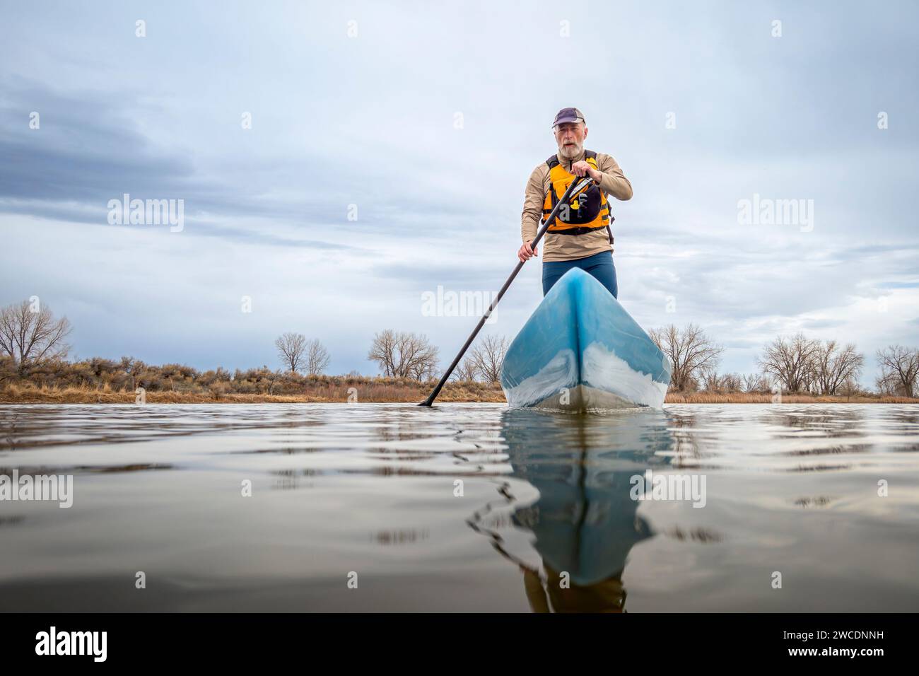 Ein älterer männlicher Paddler paddelt im Frühjahr auf einem ruhigen See mit einem Stand Up Paddleboard, aus Froschperspektive aus einer Action-Kamera auf Wasserhöhe Stockfoto