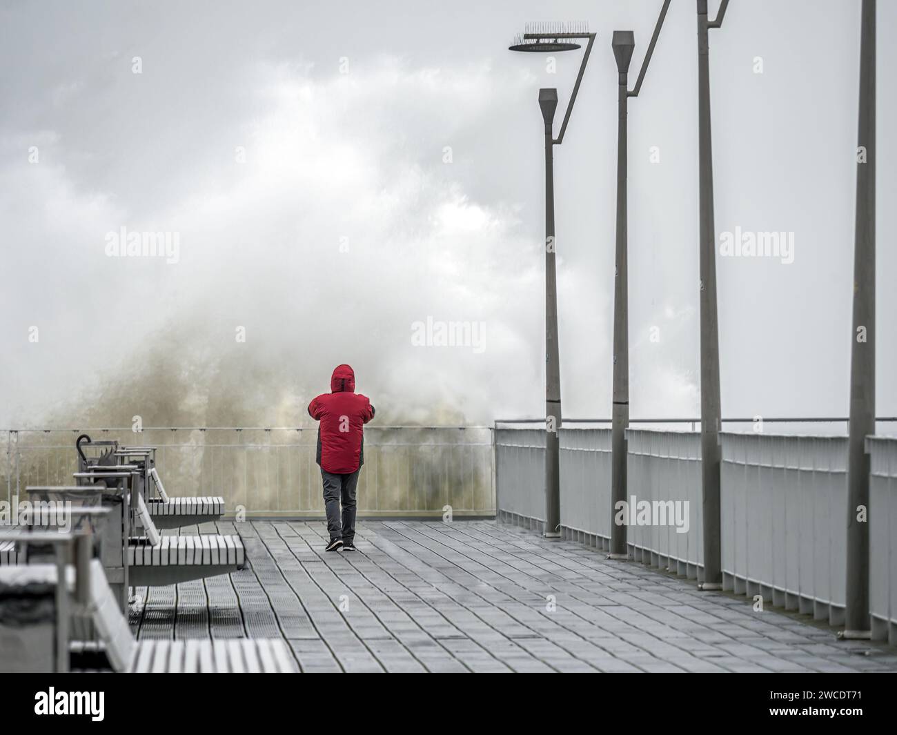 Ein Tourist, der ein Foto von einer großen stürzenden Welle macht, die die Pier-Front trifft Stockfoto