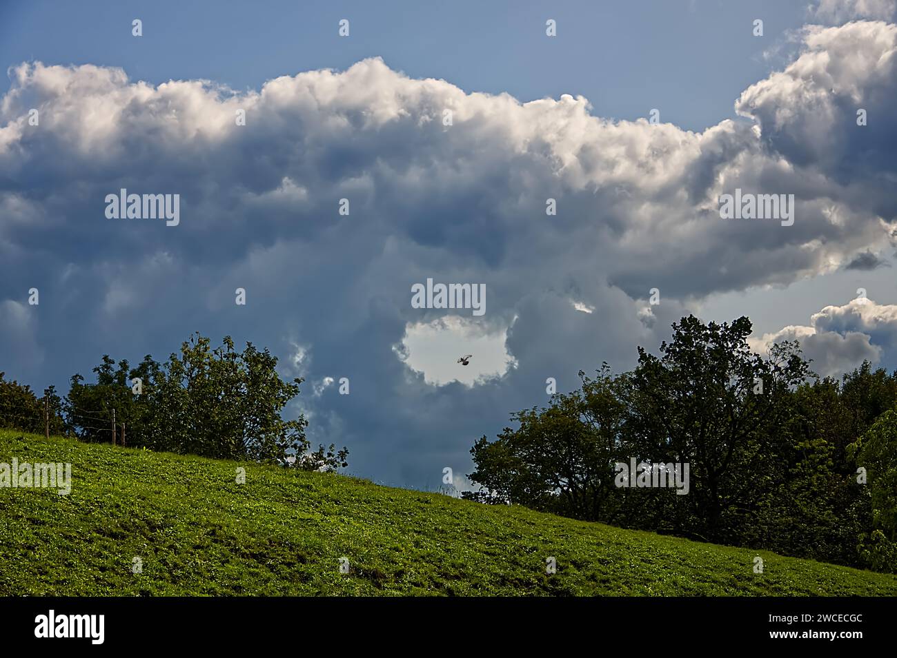 Landschaft mit bewölktem Himmel und Feldern. Die Wolken haben in der Mitte ein Loch geformt und schaffen eine dramatische und fesselnde Szene Stockfoto