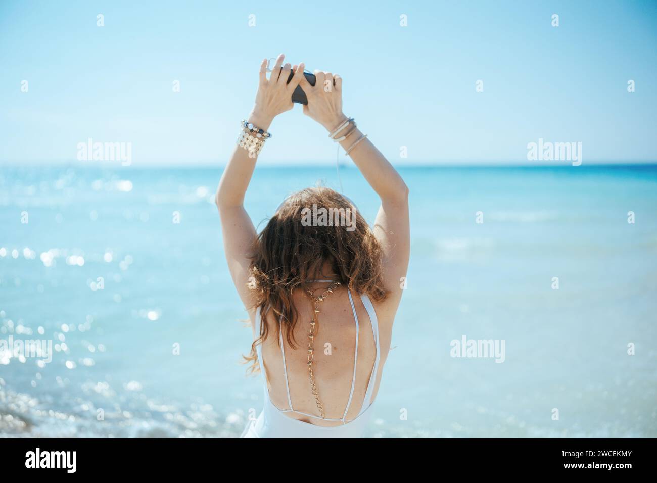 Glückliche, stilvolle Frau an der Küste mit Kopfhörern und Smartphone, die tanzt. Stockfoto