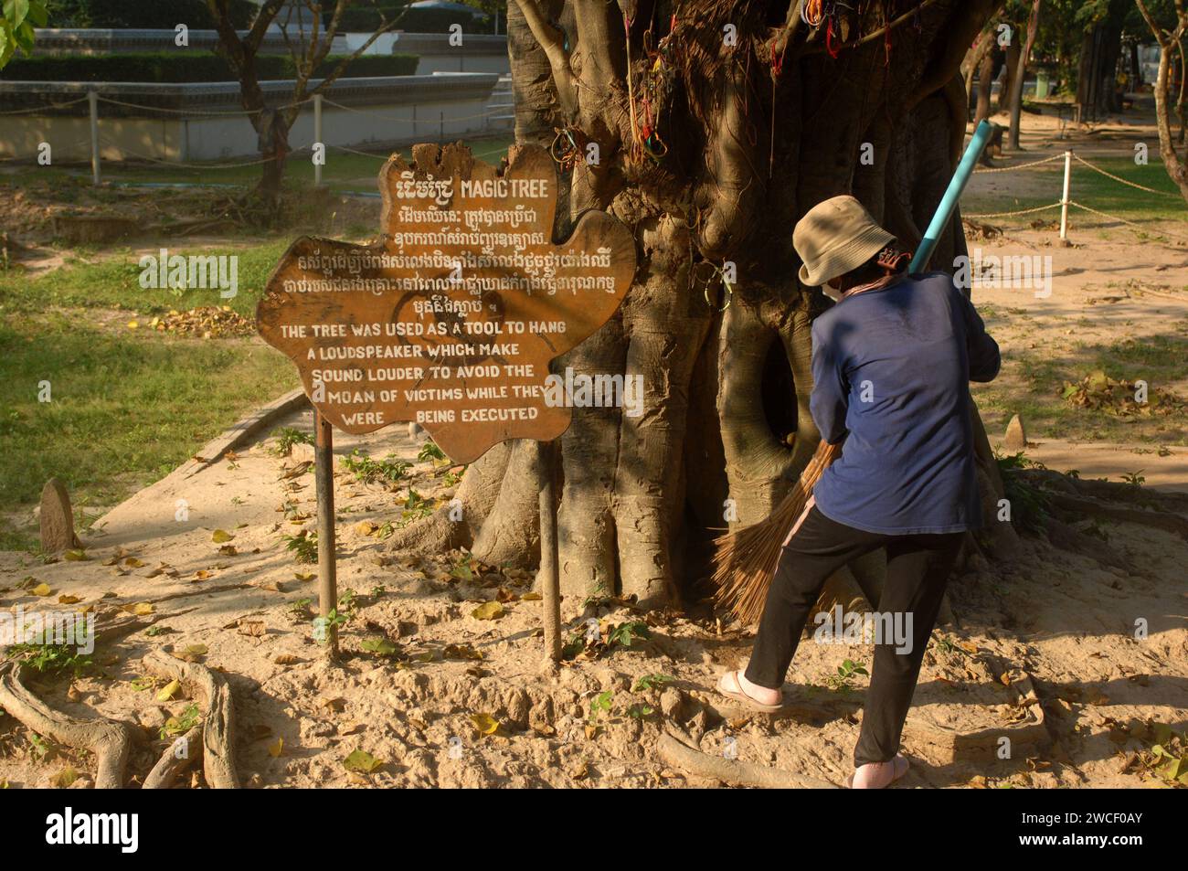 Damen fegen Blätter um einen Killing Tree in den Killing Fields des Choung EK Genocidal Center, Phnom Penh, Kambodscha. Stockfoto