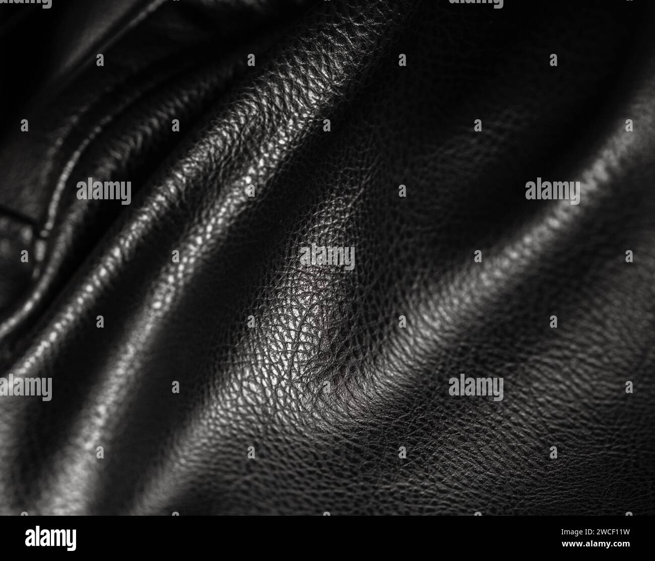 Schwarzes Leder mit Wellen und Falten. Strukturierter Hintergrund aus Kunstleder oder Kunstleder, veganes Kunstmaterial auf PVC-Basis. Nahaufnahme von Textur, Makro Stockfoto