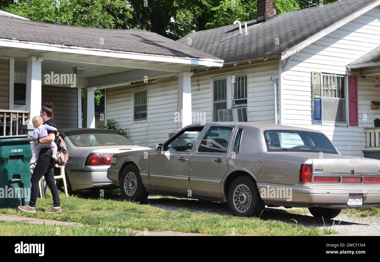 Eine Frau, die ein Baby trägt, als sie zu ihrem Haus in einer wirtschaftlich schwierigen Gegend von Springfield Missouri geht, ein Lincoln Towncar parkte in ihrer Einfahrt - M Stockfoto
