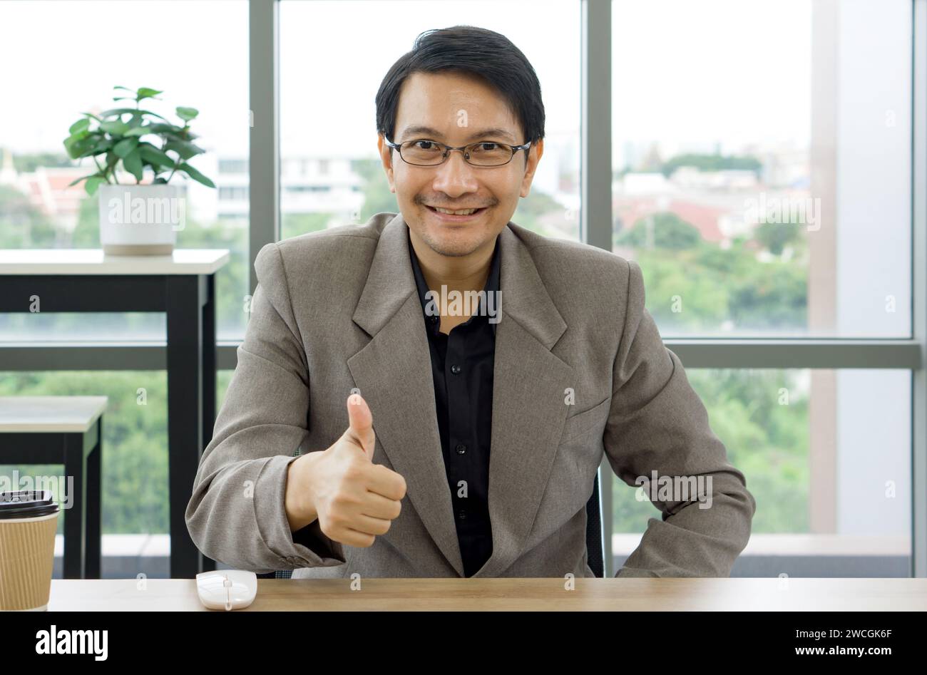 Ein Mann, der einen formellen Anzug trägt, lächelt und zeigt ein Schild mit den Daumen hoch mit der Hand, um seine Zustimmung auszudrücken. Stockfoto