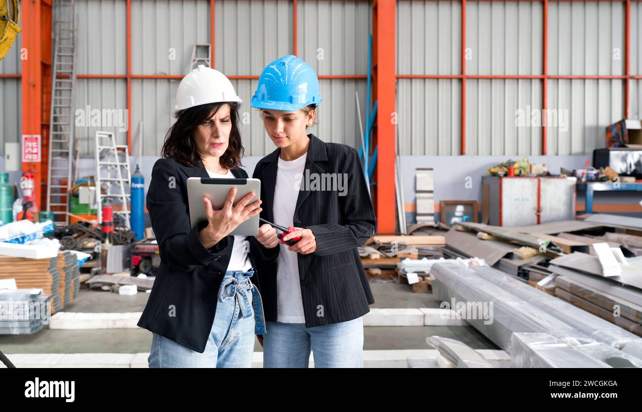 Zwei Frauen mit Schutzhelm stehen in einem Lager, inspizieren den Bestand oder überwachen den Betrieb. Stockfoto