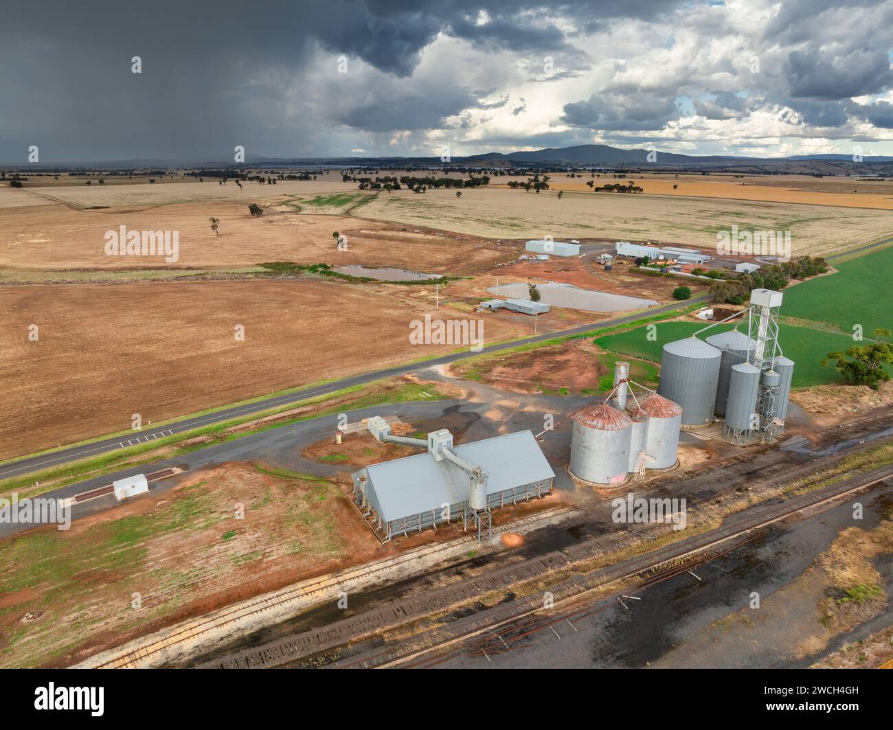 Aus der Vogelperspektive auf Getreidesillos entlang einer ländlichen Eisenbahnlinie mit dunklen Wolken und Regen in der Ferne bei Moolort in Central Victoria, Australien. Stockfoto