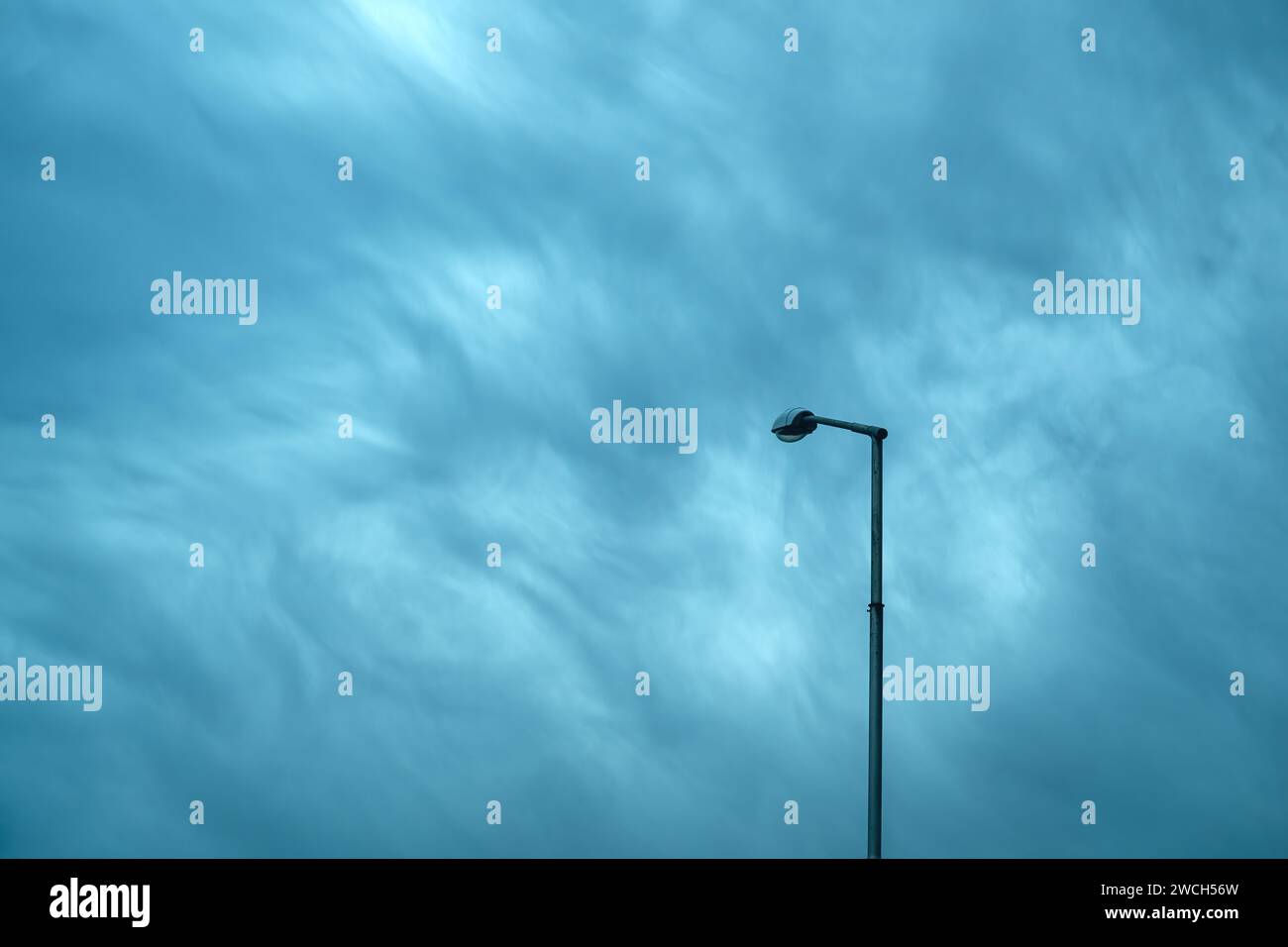 Straßenlaterne an einem hohen Pfosten vor stimmungsvollem, dramatischem Himmel, minimalistische Komposition Stockfoto