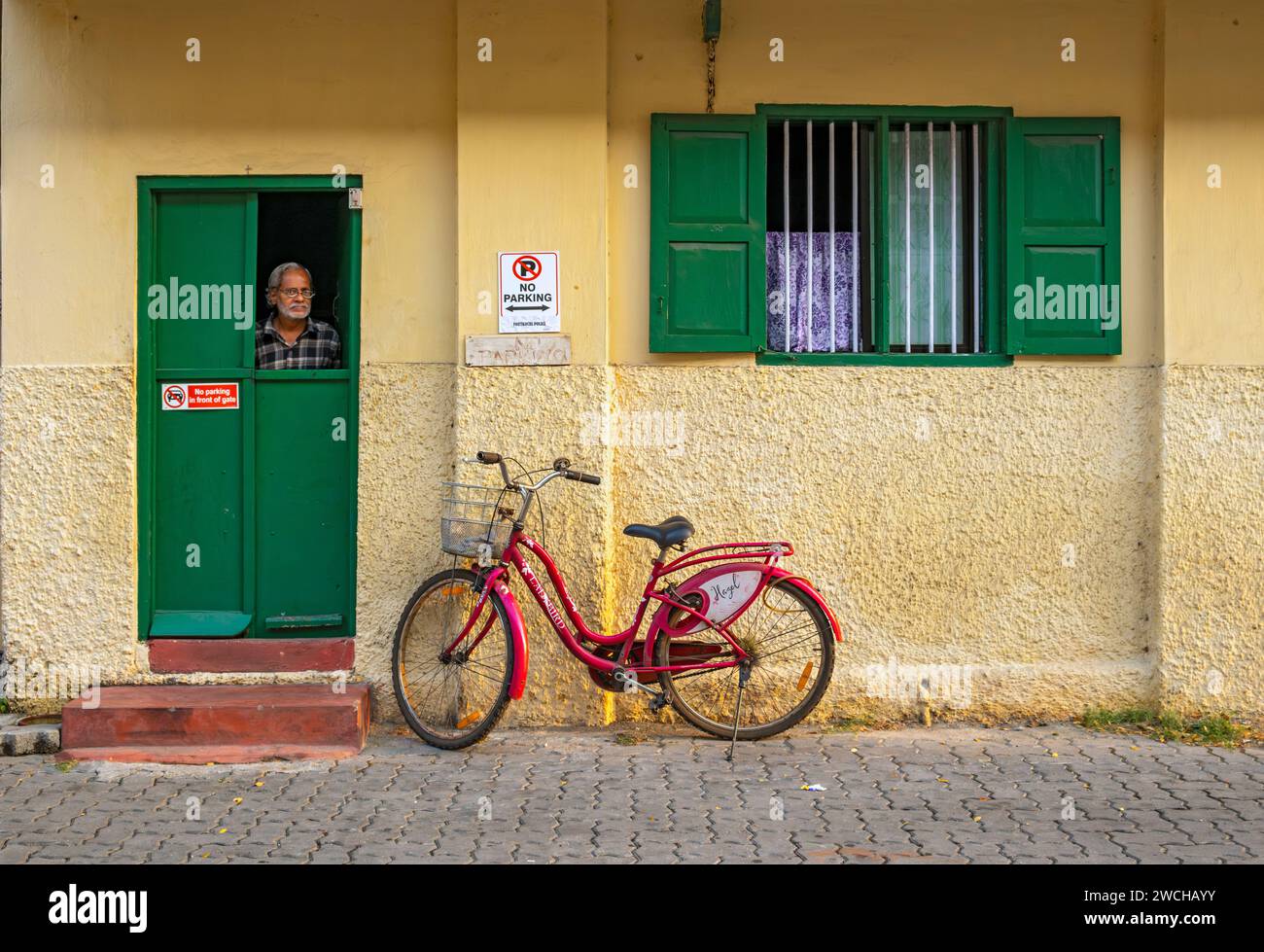 Der Mann schaut aus einem gelben Haus mit rotem Fahrrad, Fort Kochi, Cochin, Kerala, Indien Stockfoto