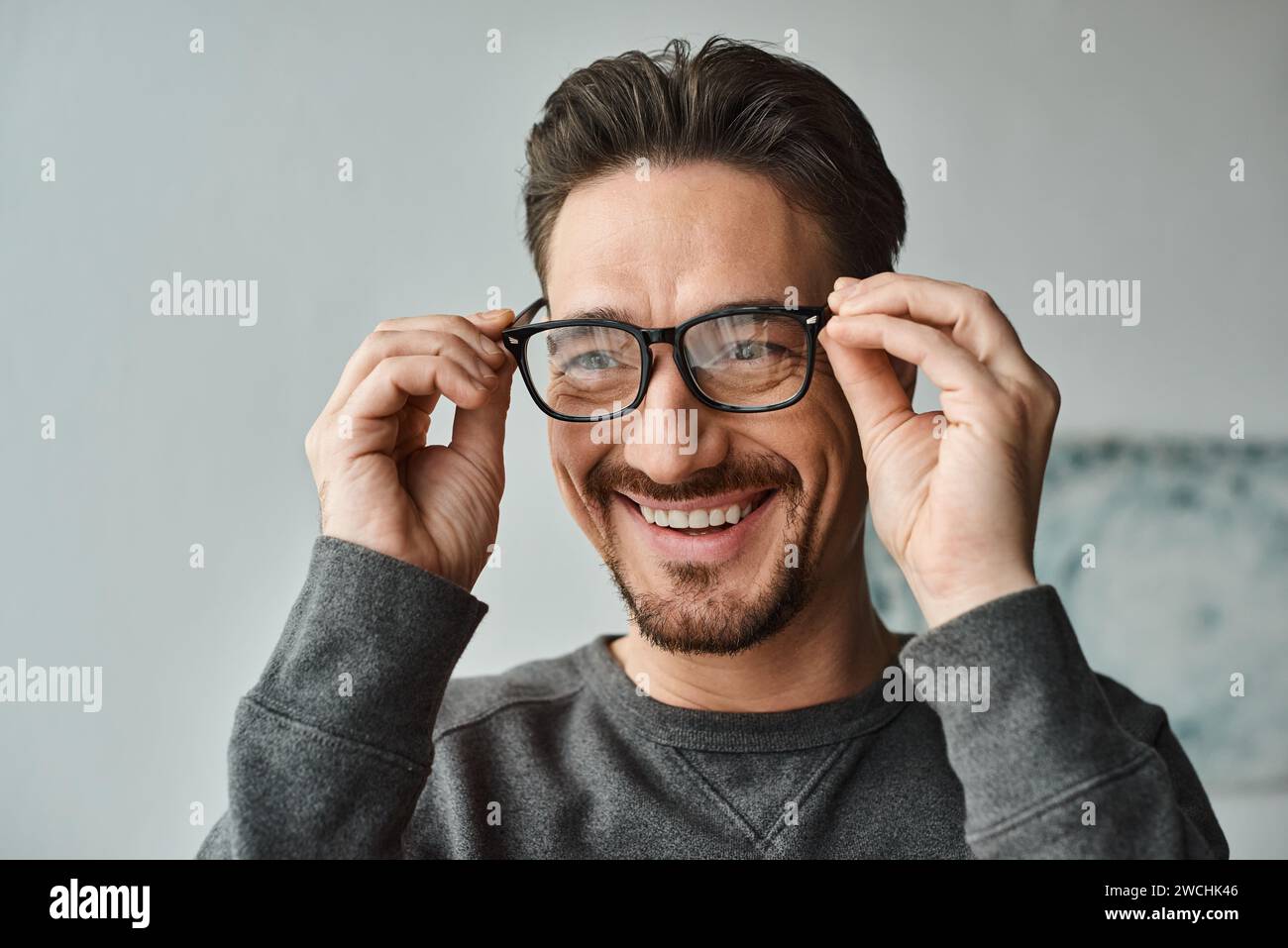 Porträt eines fröhlichen und bärtigen Mannes im grauen Pullover mit Brille und Blick in die Kamera Stockfoto