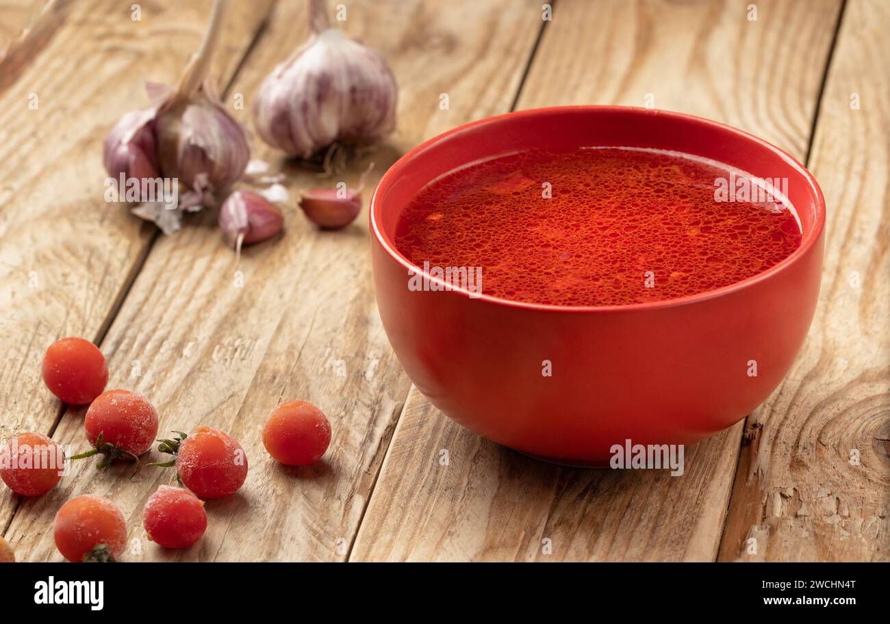 Tomatensuppe auf einem Holztisch mit Kirschtomaten und Knoblauchköpfen. Stockfoto