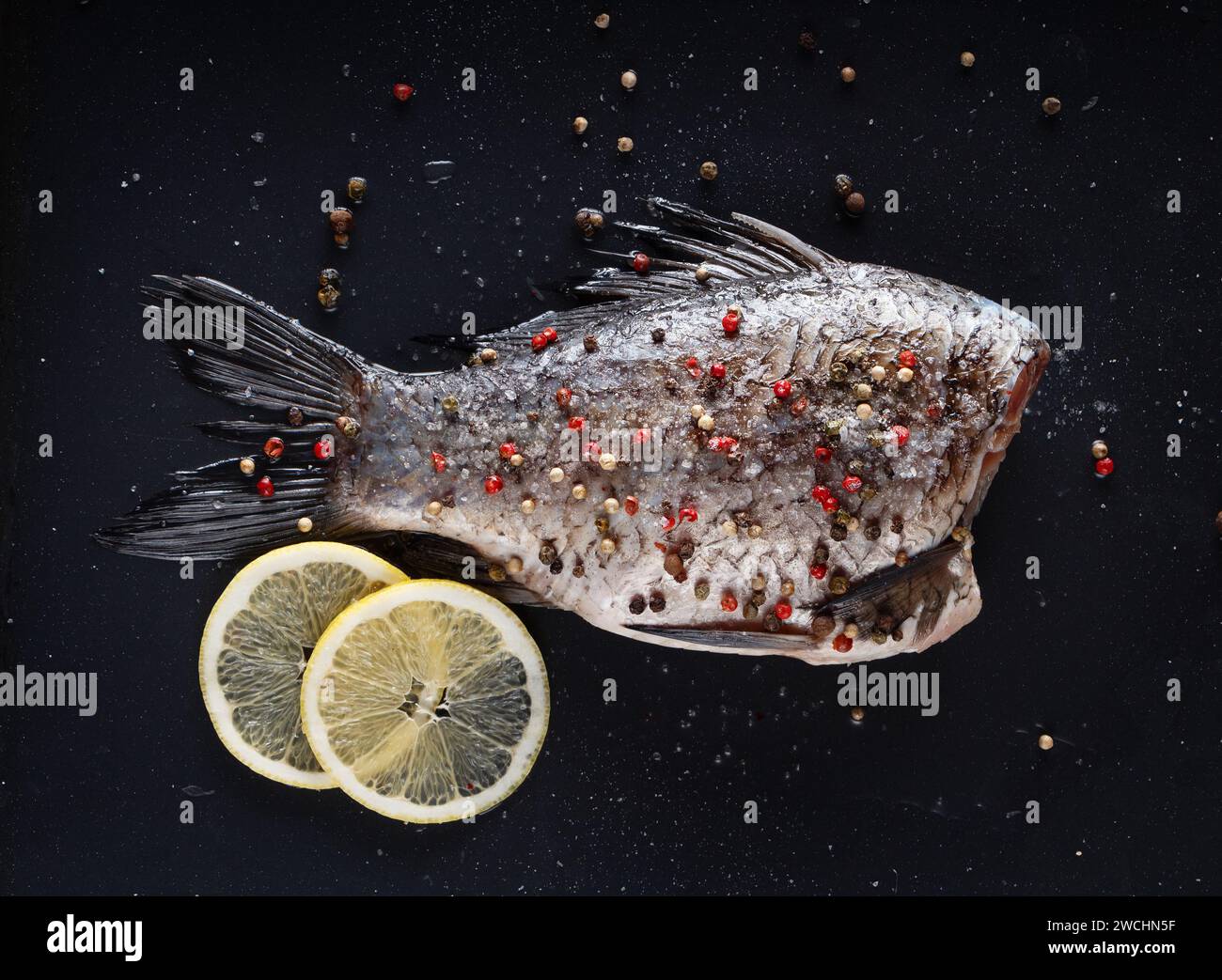 Karpfen zum Backen mit Pfeffer, Salz und Zitronen auf schwarzem Hintergrund. Stockfoto