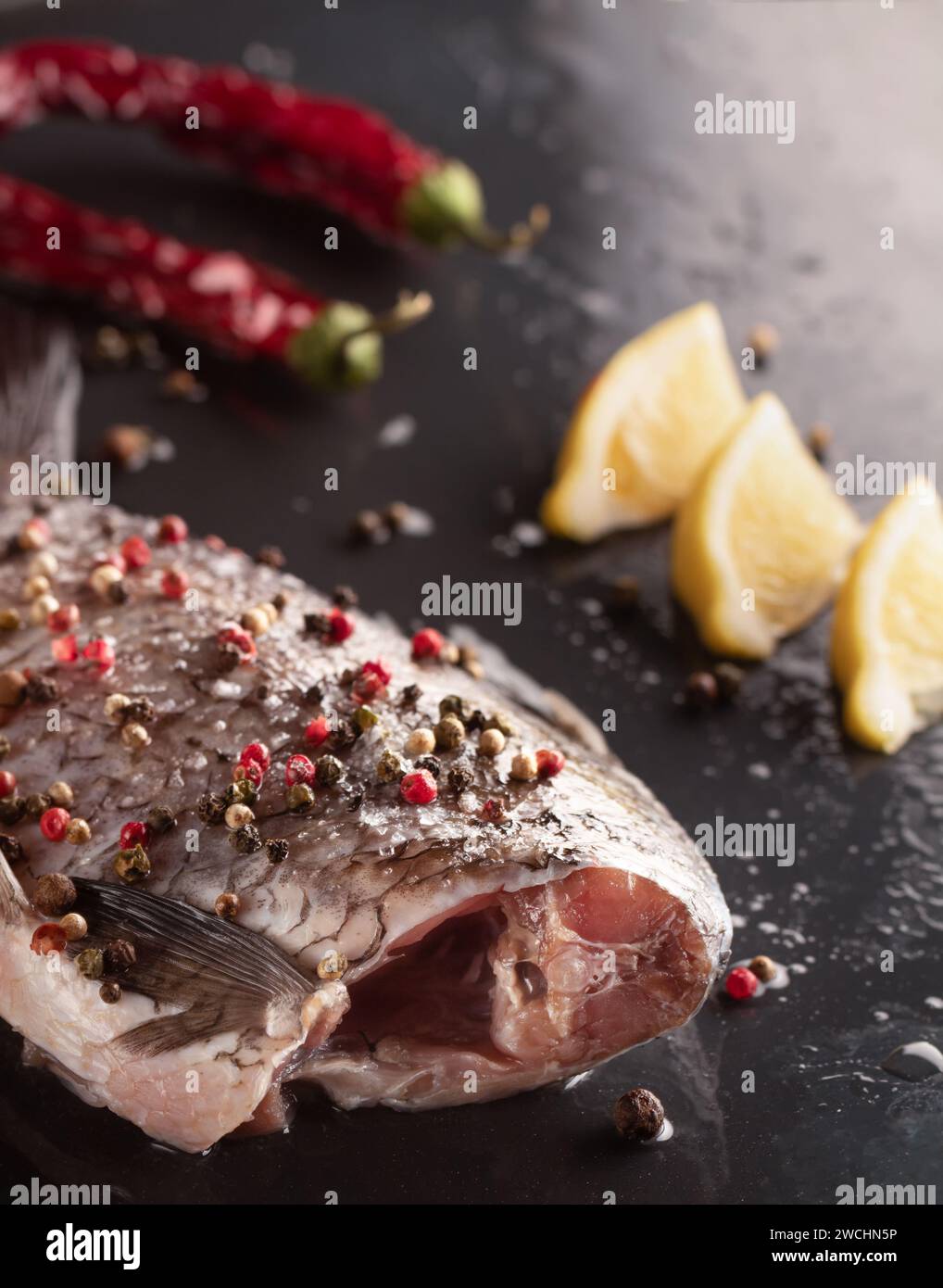 Karpfen zum Backen mit Pfeffer, Salz und Zitronen auf schwarzem Hintergrund. Stockfoto