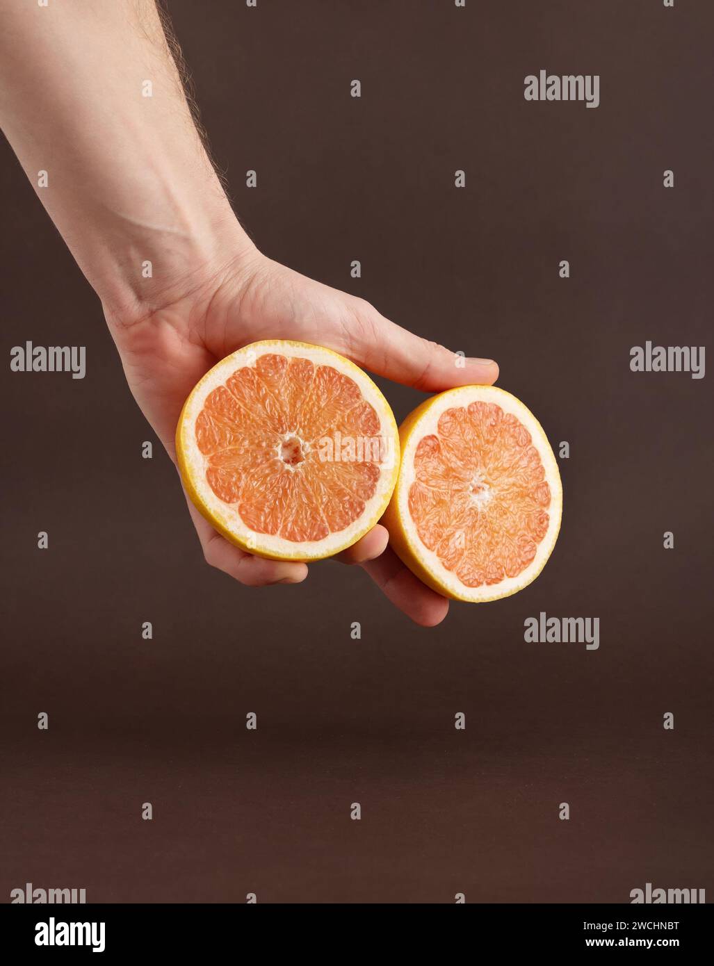 Zwei Hälften einer geschnittenen Grapefruit auf der Hand des Mannes auf braunem Hintergrund. Stockfoto