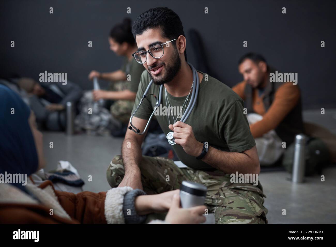 Porträt eines lächelnden Mannes aus dem Nahen Osten als Militärarzt, der mit Flüchtlingen spricht und Gesundheitsuntersuchungen in Unterkünften, Kopierräumen durchführt Stockfoto