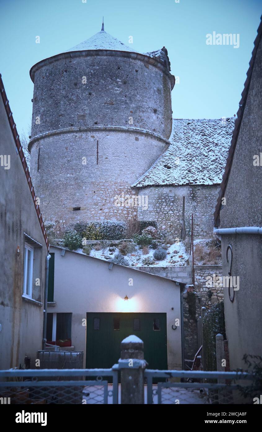 Ein Vintage-Turm mit einem lebhaften grünen Eingang, der sich inmitten benachbarter Gebäude in Saint-Loup-de-Naud befindet Stockfoto