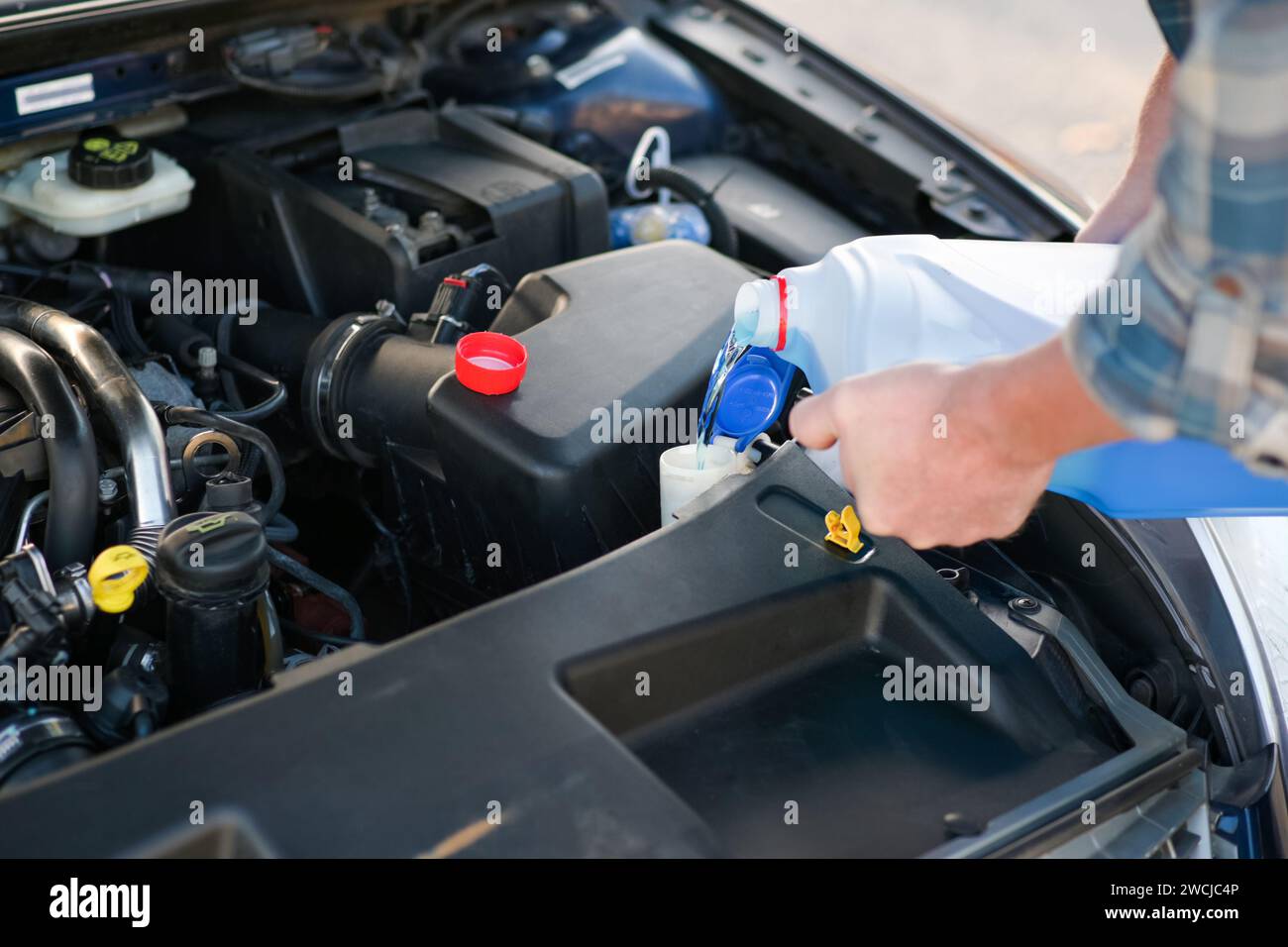 Der Mechaniker fügt den Waschanlagen Wasser hinzu, kümmert sich um das Fahrzeug, die Nahaufnahme und den unscharfen Hintergrund. Stockfoto
