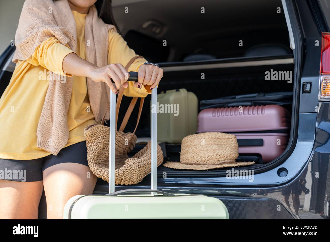 Eine junge Frau bereitet sich darauf vor, ihre Reisetasche hinten im Auto zu laden, um sich auf eine Urlaubsreise vorzubereiten Stockfoto