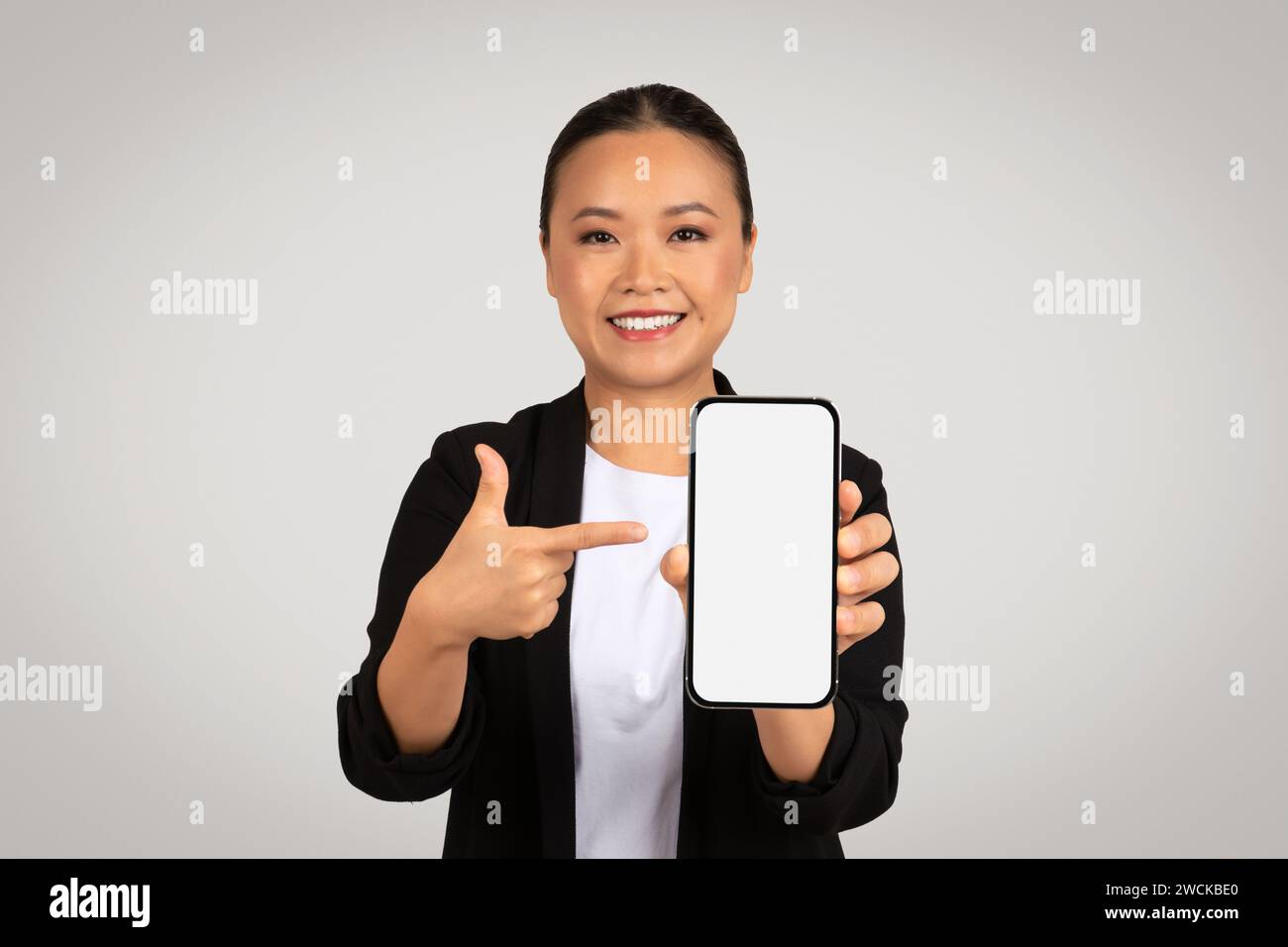 Selbstbewusste asiatische Geschäftsfrau, die ein Smartphone mit einem leeren weißen Bildschirm präsentiert Stockfoto
