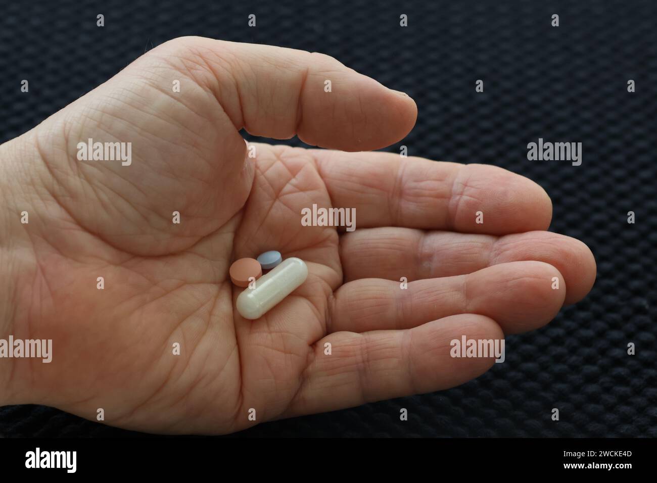 Eine Hand, die eine tägliche Dosis von drei Tabletten auf dunklem Hintergrund hält Stockfoto