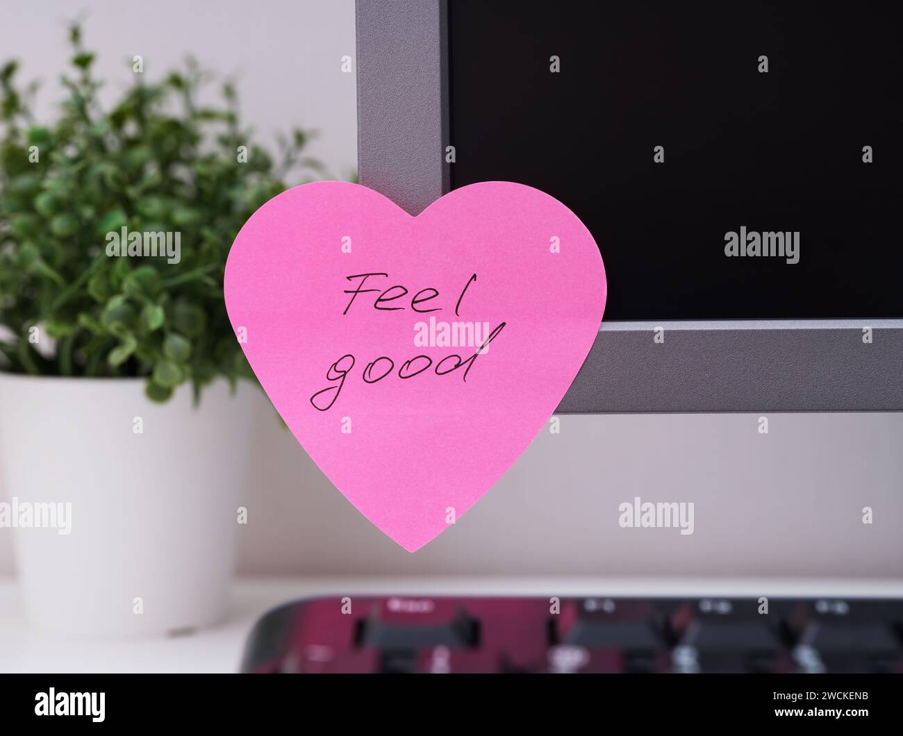 Ein rosafarbener, herzförmiger Papierschein mit Worten, die sich gut anfühlen, ist an einem Arbeitsplatz am Monitor angebracht. Stockfoto