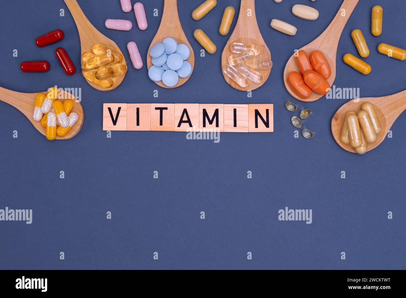 Verschiedene Vitamine in Holzlöffeln mit Text auf grauem Hintergrund. Pillen, Medikamente, Nahrungsergänzungsmittel, Medizin, Apotheke und Gesundheitskonzept. Stockfoto