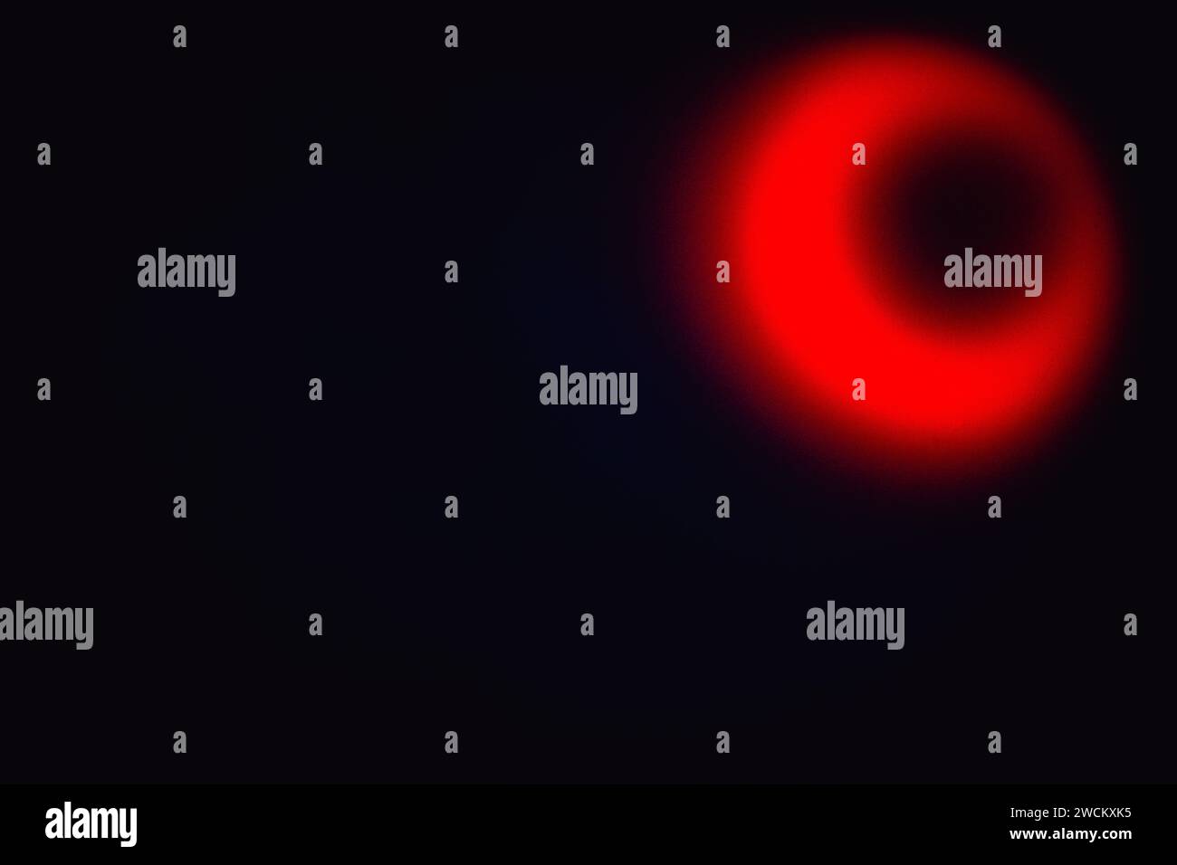 Elliptische Form von hellrotem, unscharfem Licht mit einem dunklen Loch im Inneren auf schwarzem Hintergrund Stockfoto