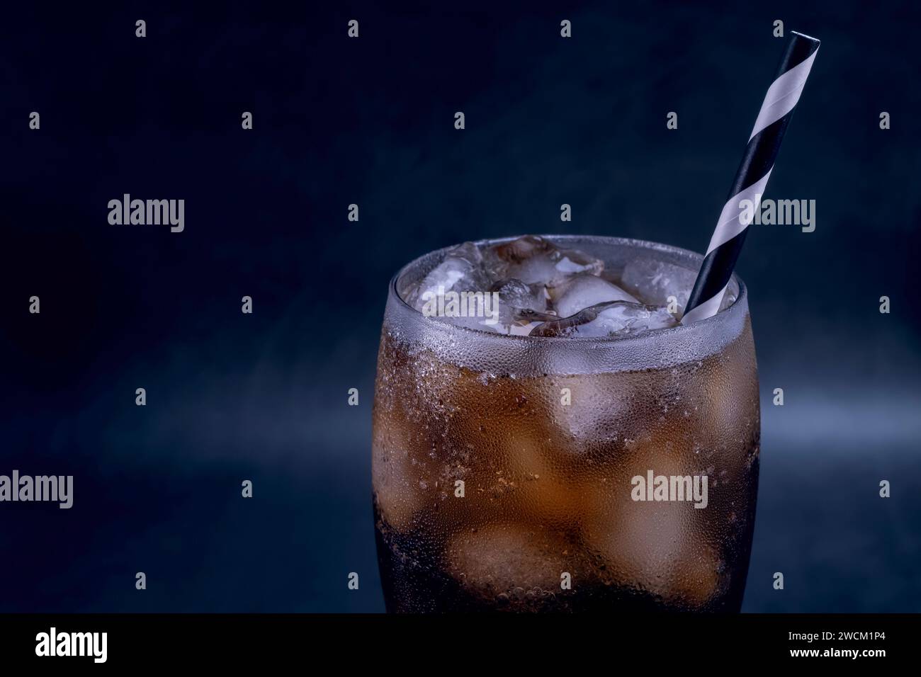 Kühles Glas Cola mit Eis, Blasen und Fizz. Frisches, kaltes Süßes mit Eiswürfeln. Cola-Glas mit Sommererfrischung auf Schwarz. Stockfoto