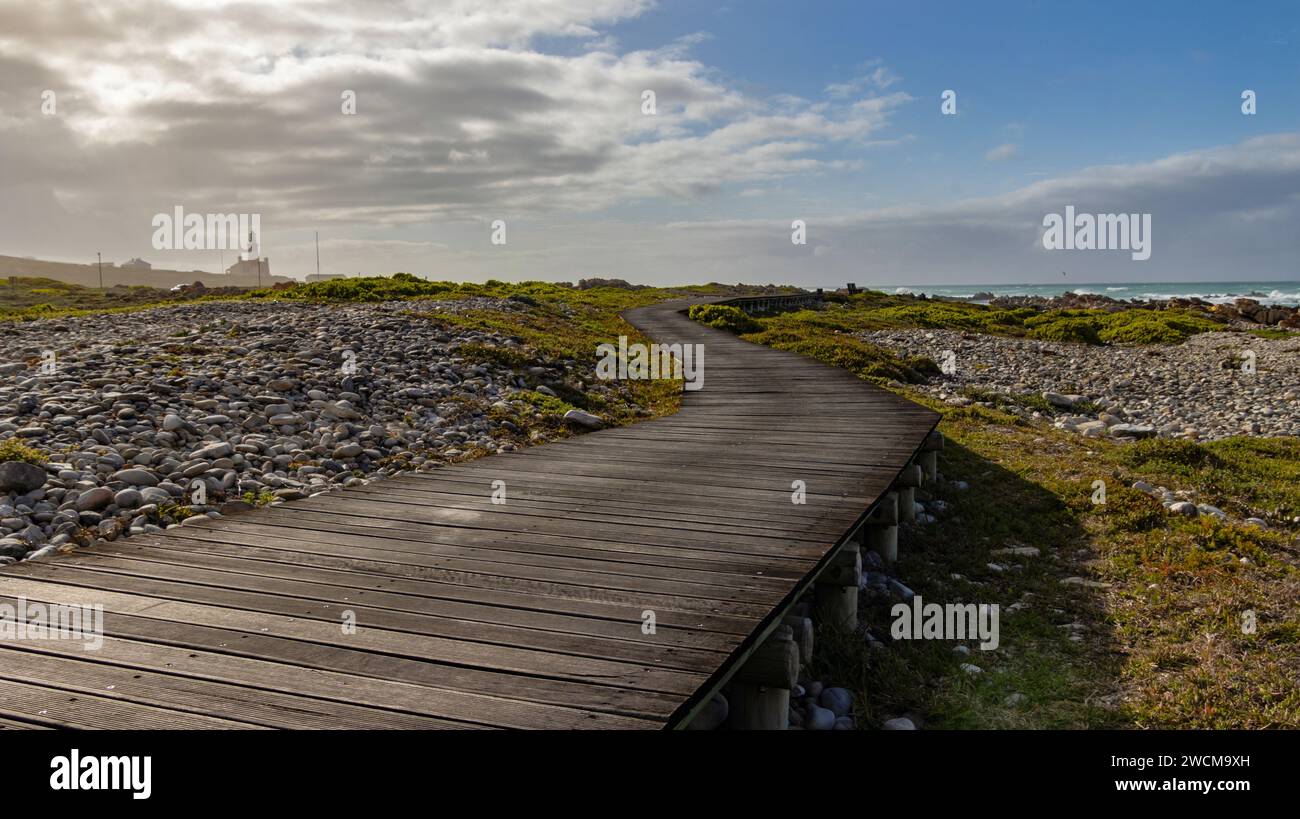 Ein malerischer Weg führt zu einem Sandstrand, der sich zum sprudelnden Wasser erstreckt und eine ruhige und einladende Atmosphäre schafft Stockfoto