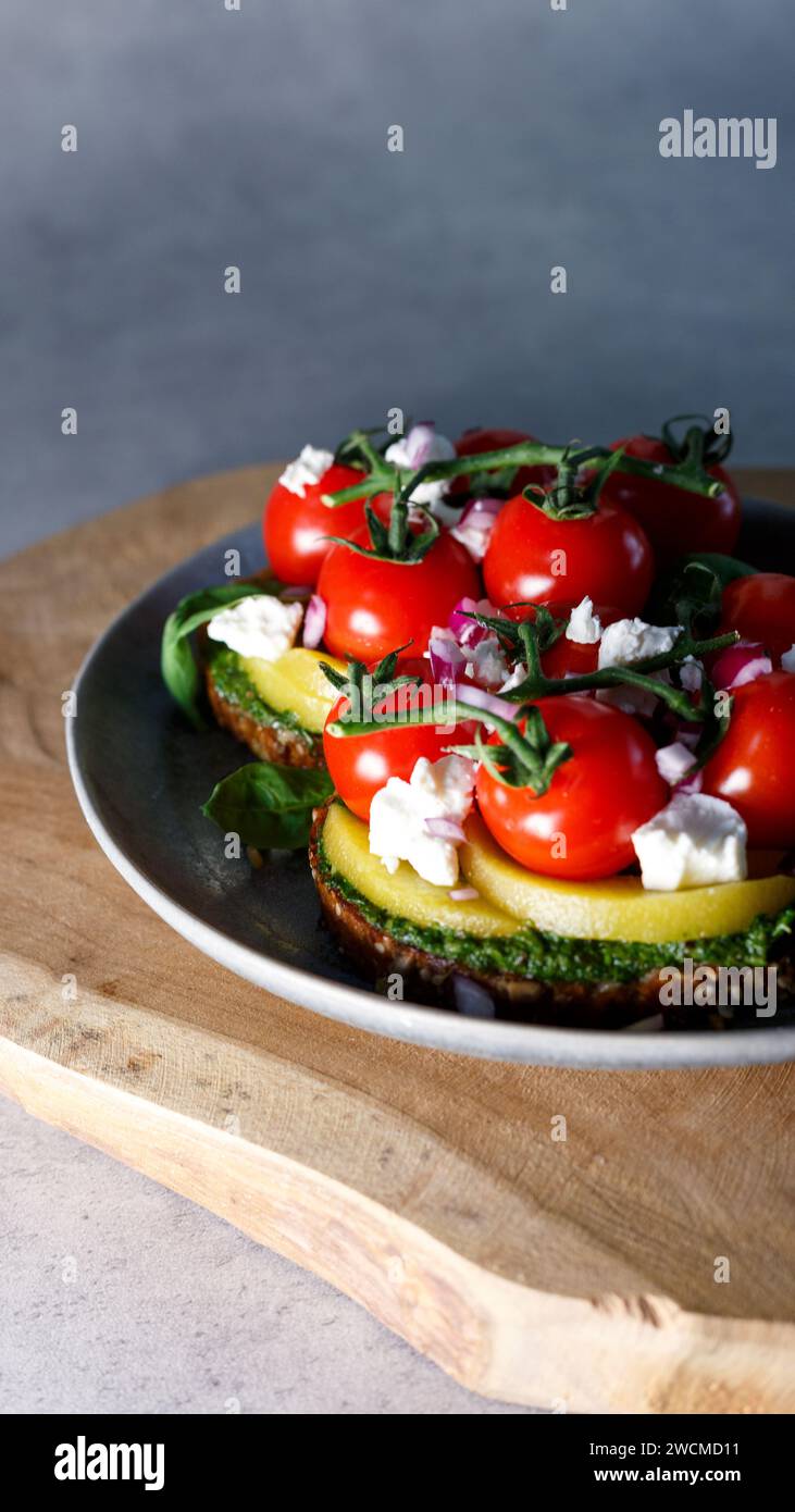 Ein elegant präsentiertes vegetarisches Gericht mit Reifen Kirschtomaten, cremigen Avocadoscheiben und zerbröckeltem Käse auf knusprigem Toast, bereit für den Genuss der SE Stockfoto