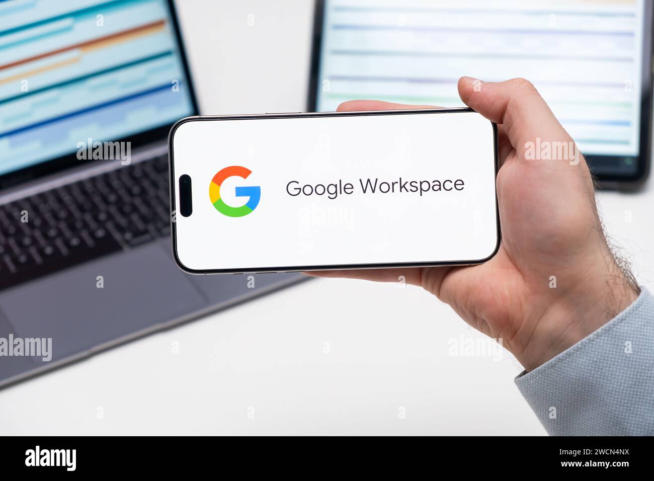 Google Workspace-Anwendungslogo auf dem Bildschirm des Smartphones in der Hand, Laptop und Tablet sind auf dem Tisch im Hintergrund, Dezember 2023, Prag, Tschechische Republik. Stockfoto