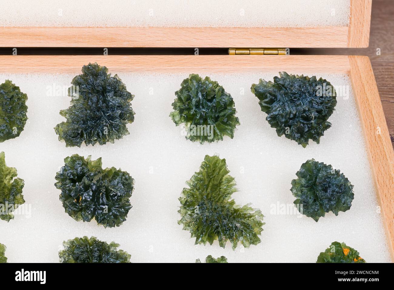 Nahaufnahme einer Sammlung roher grüner Moldavit-Edelsteine im hölzernen Vorratsschrank. Gruppe des seltenen glasigen Kieselsäure-Tektitminerals mit Ursprung in Südtschechien. Stockfoto