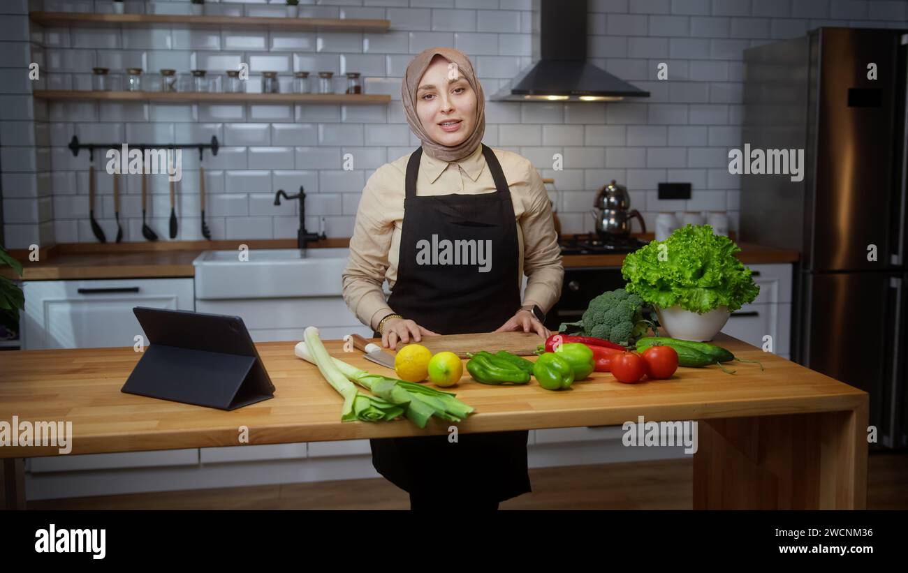 Vlogger-Chefkoch mit Kopftuch auf einer Schürze, die Videokochstunde über vegetarische Gerichte oder Salate in der modernen Küche zu Hause aufnimmt. Online-Übertragungen Stockfoto