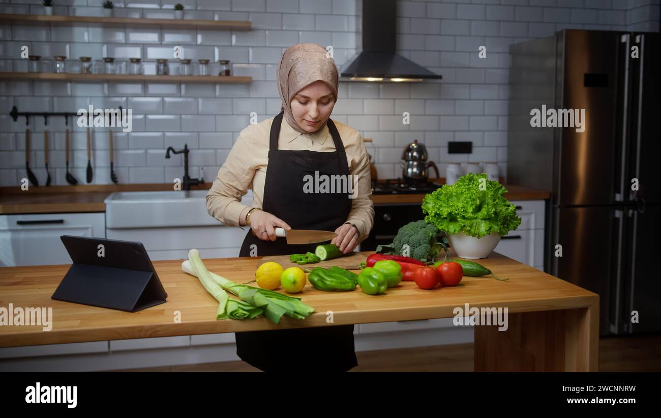 Vlogger junge Chefkochin mit Kopftuch auf der Schürze Aufnahme Video Kochkurs über vegetarische Gerichte oder Salate in der modernen Küche zu Hause. Online b Stockfoto