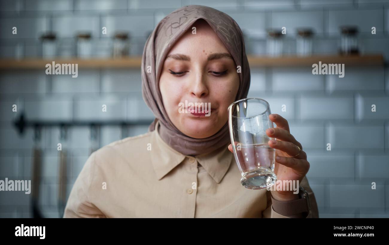 Eine junge Kopftücher-Frau, die ihre Medizin nimmt, während sie in der Küche sitzt Stockfoto