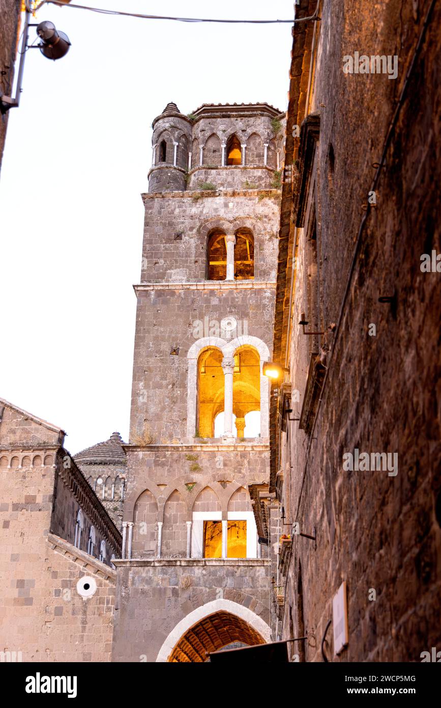 Bild eines Glockenturms in der Nähe einer Kirche mit beleuchteten Fenstern, aufgenommen in Caserta Vecchia, Italien Stockfoto