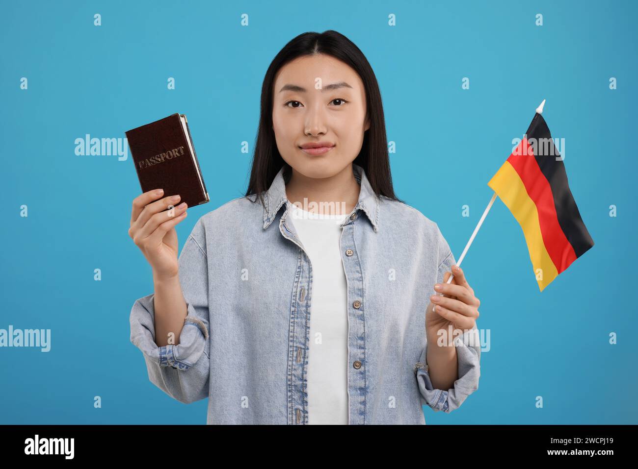 Einwanderung nach Deutschland. Frau mit Pass und Flagge auf hellblauem Hintergrund Stockfoto