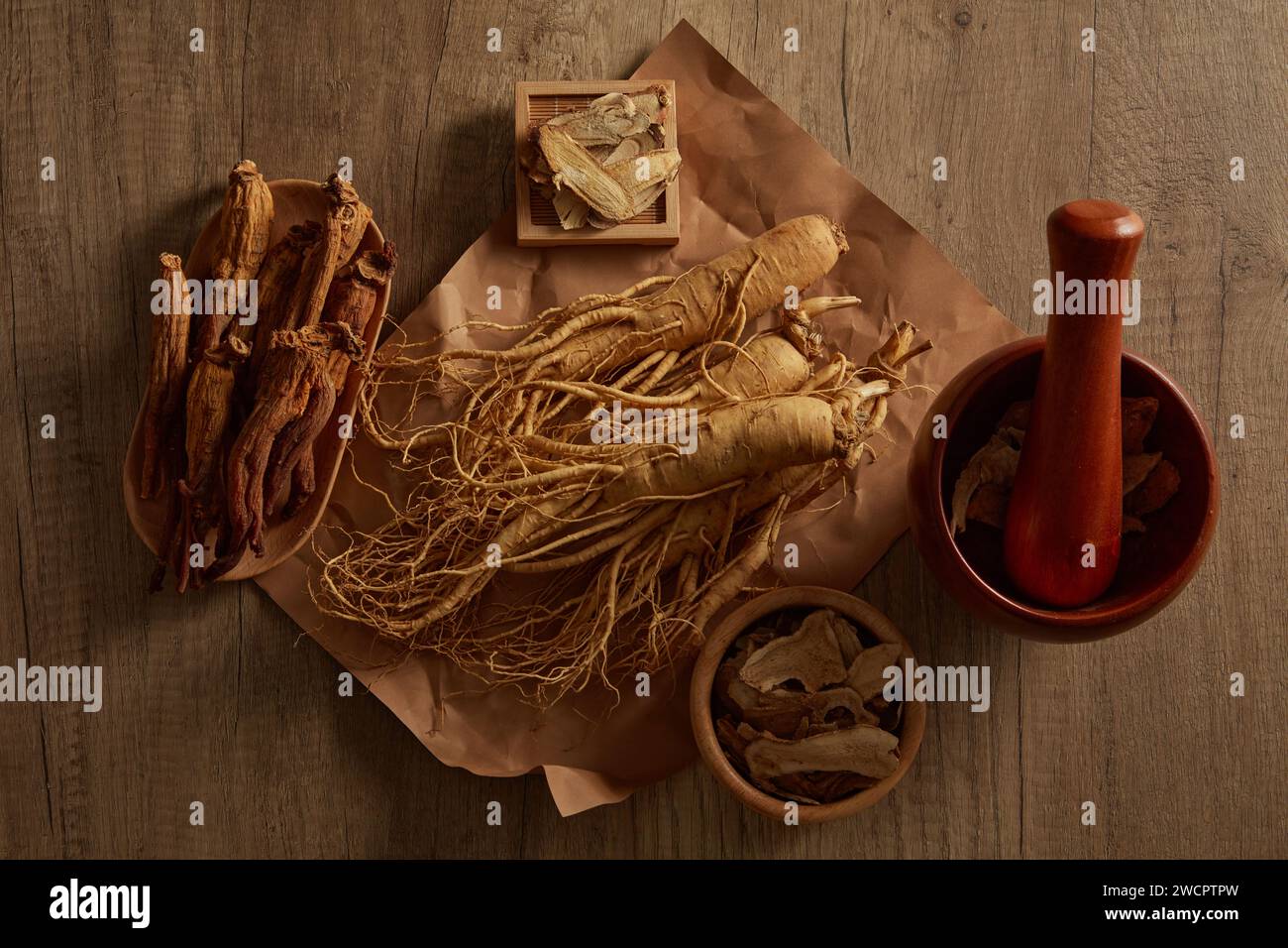 Mehrere Ginseng-Wurzeln wurden auf ein Papier gelegt und mit einer Schale aus rotem Ginseng, Bai zhu und Rhabarber gezeigt. Kräuter sind selten und haben die Fähigkeit, Gesundheit zu behandeln Stockfoto