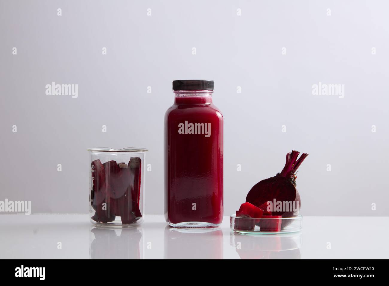 Eine Glasflasche ohne Etikett, gefüllt mit Rote-Bete-Saft. Becher und Petrischale mit Rote-Bete-Scheiben angezeigt. Rote Bete (Beta vulgaris) kann die musc verbessern Stockfoto