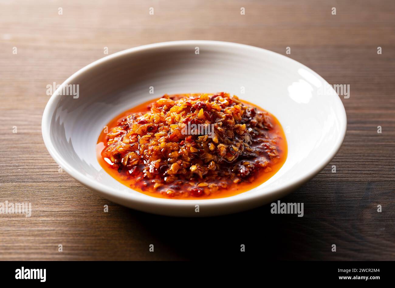Ein essbares Chili-Öl in einer Keramikschale auf hölzernem Hintergrund. Stockfoto