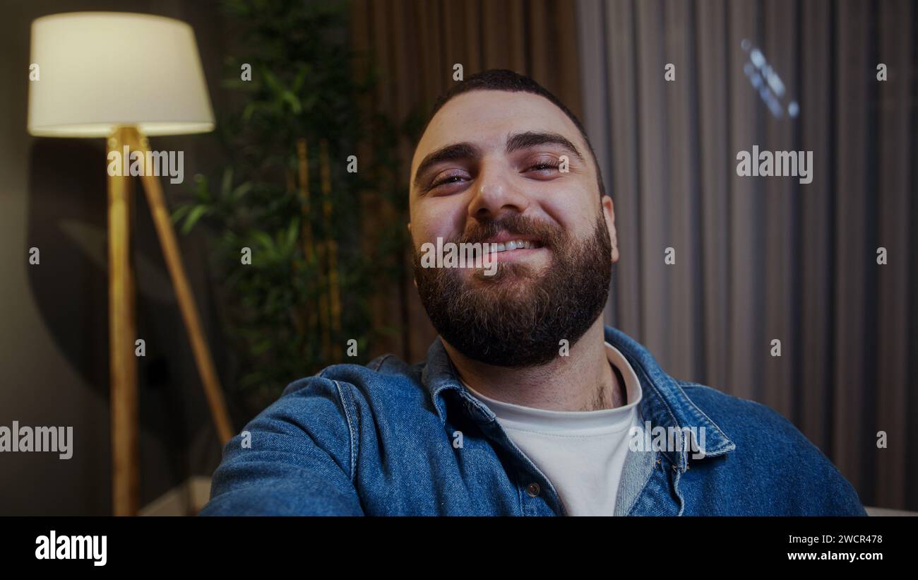 Selfie eines lächelnden jungen erwachsenen Mannes, der ein Smartphone in der Hand hält, in die Kamera schaut und Fhoto macht Stockfoto