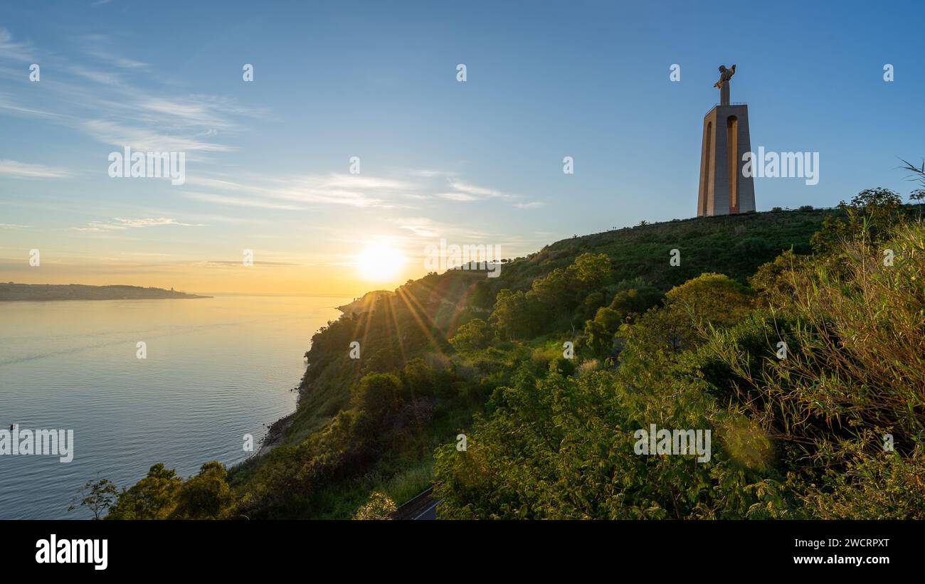 Statue Christi in Almada/Lissabon, mit Sonnenuntergang auf der geteerten Straße und dem Fluss Tejo Stockfoto