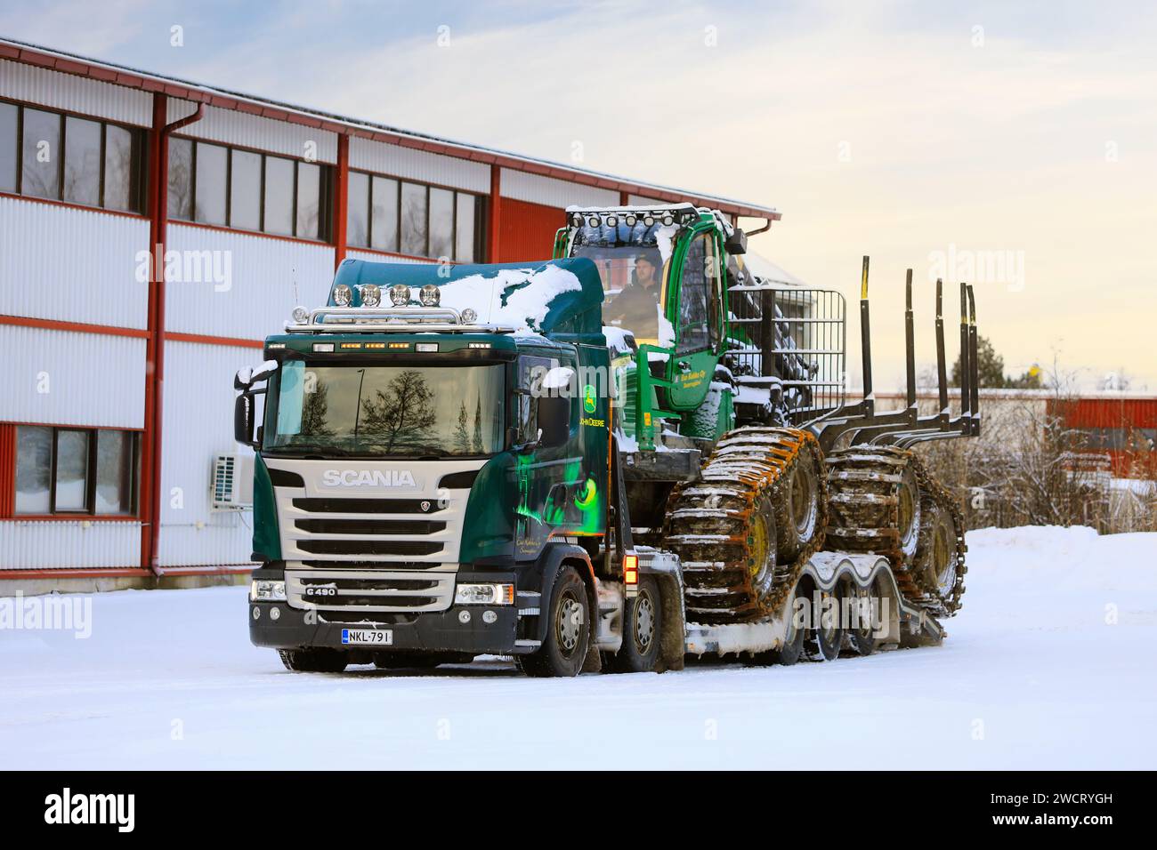 Verladung des John Deere 1210E Forstförderers auf den Scania G490 Lkw-Anhänger für den Transport an einem Wintertag. Salo, Finnland. Dezember 2023. Stockfoto