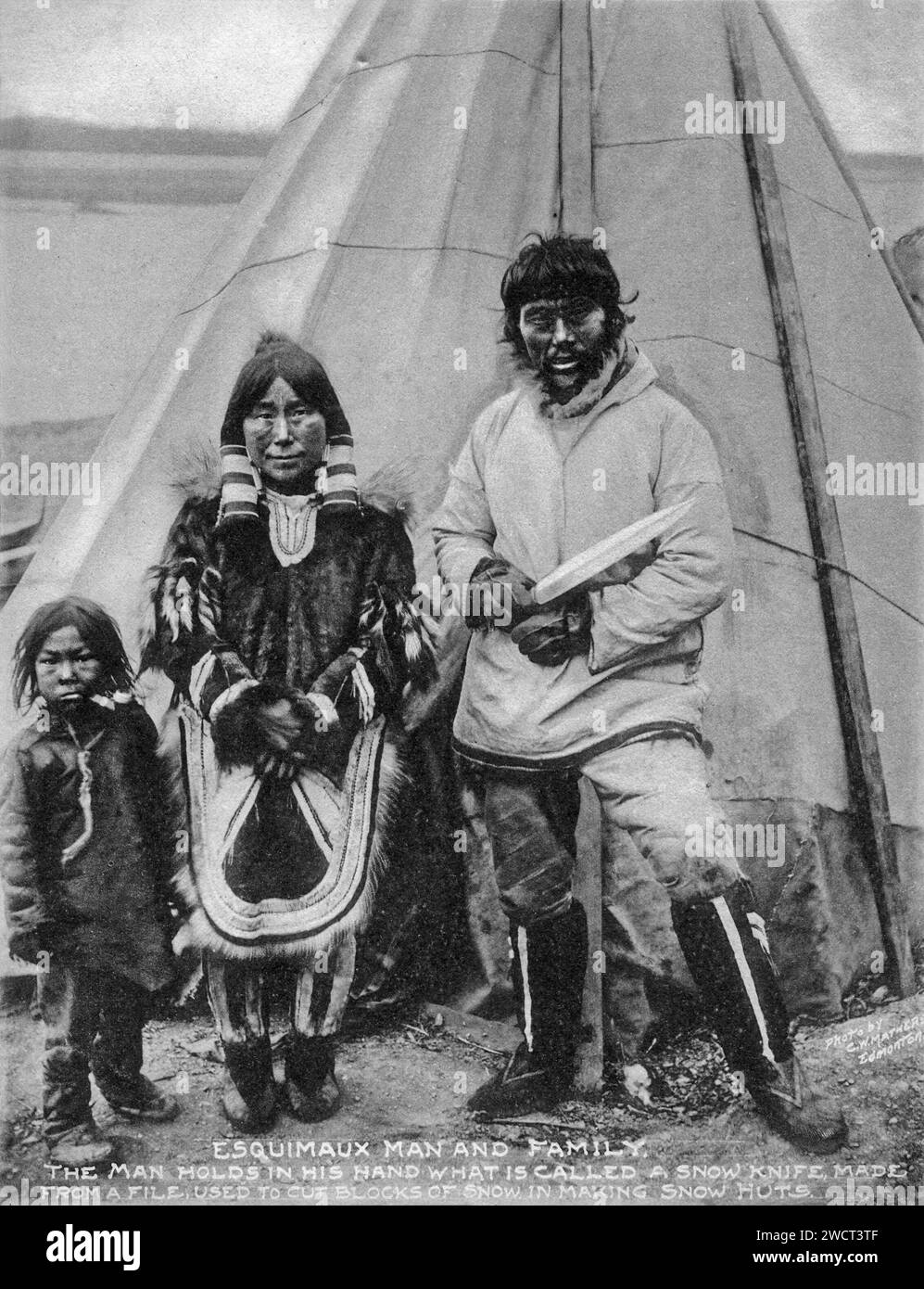 Ein Foto einer Inuit-Familie aus dem Jahr 1901, aufgenommen von C W Mathers auf einer Expedition in den hohen Norden Kanadas und veröffentlicht in seinem Buch „The Far North“. Mathers untertitelte dieses Foto: Eskimaux [Inuk] Mann und Familie. Der Mann hält in der Hand ein so genanntes Schneemesser, das aus einer Feile hergestellt wird, um Schneeblöcke zu schneiden, um Schneehütten [Iglus] zu bauen. Stockfoto