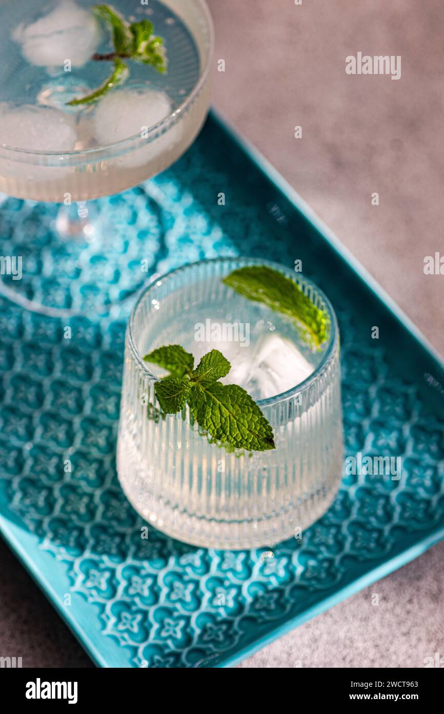 Zwei erfrischende Cocktails mit Minzgarnitur, Eiswürfel auf einem blau gemusterten Tablett, elegante Gläser Stockfoto