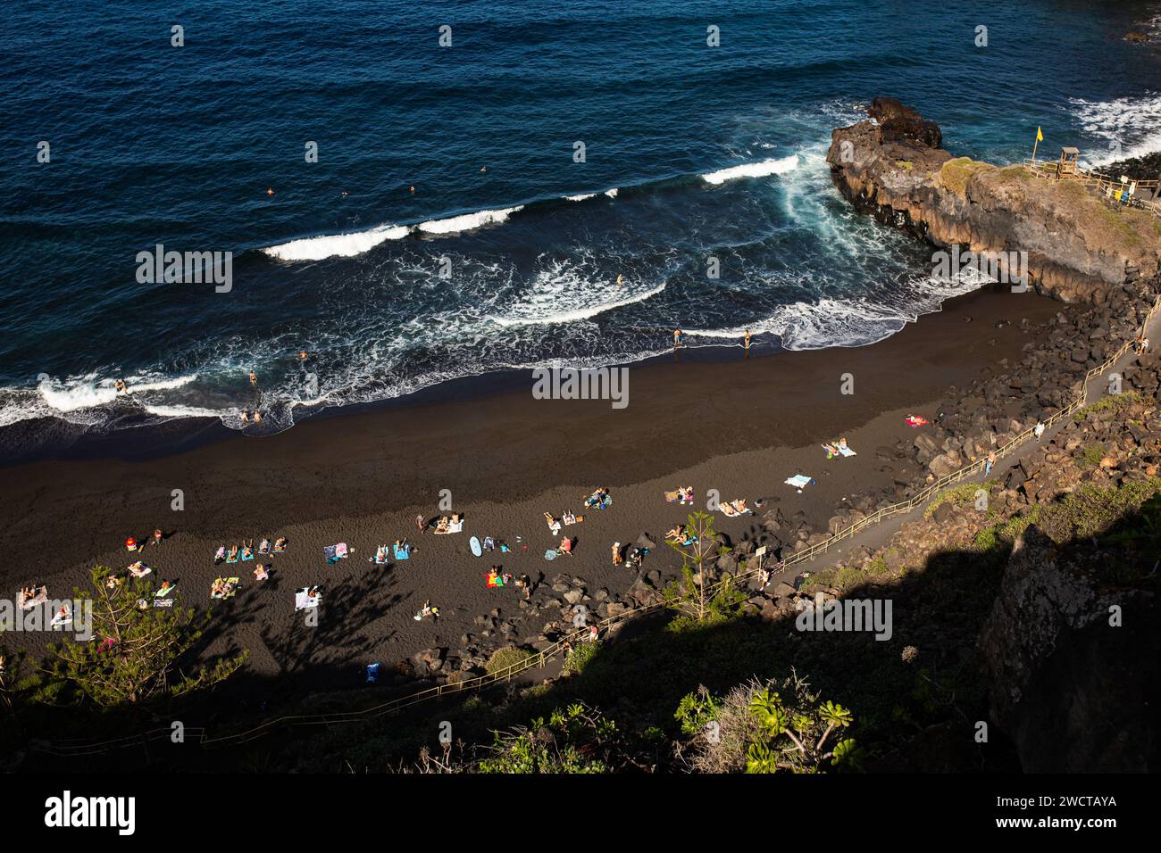 Touristen und Einheimische genießen einen sonnigen Tag an einem einzigartigen schwarzen Sandstrand, umgeben von zerklüfteten Klippen und Atlantikwellen Stockfoto